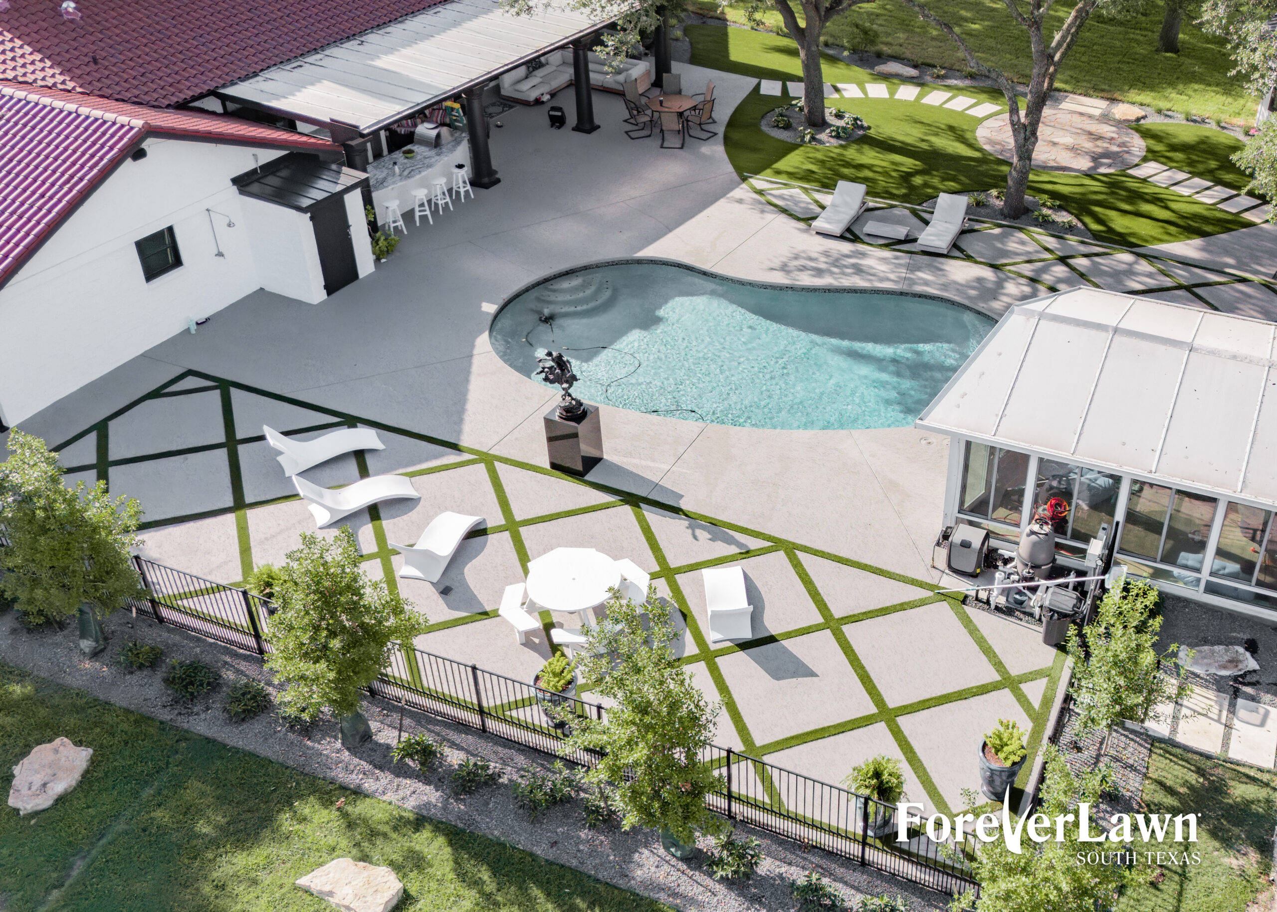 A modern, curvy pool with a spa, surrounded by a gray deck and potted plants, set against a backdrop of open fields and dark clouds